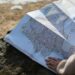 A person studies a roadmap placed on a rock, embraced by natural sunlight outdoors.